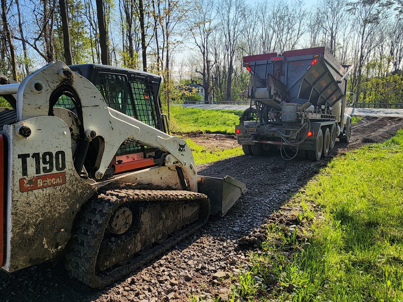 New gravel driveway installation - skid steer and stone spreader at work